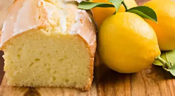 Un délicieux moelleux au citron, avec un glaçage blanc et des citrons frais sur une planche en bois.