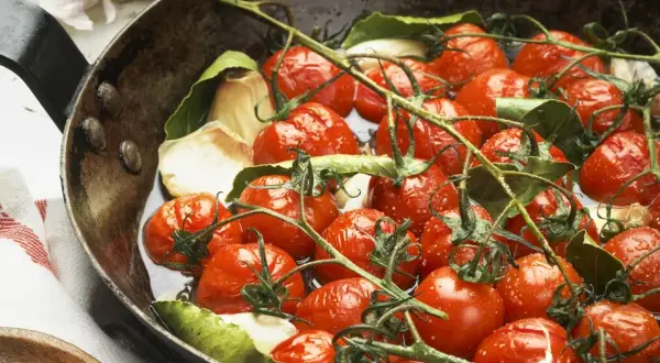 Saftige cherry tomaten mit Knoblauch und Lorbeerblättern in einer Pfanne, bereit zum Garen.