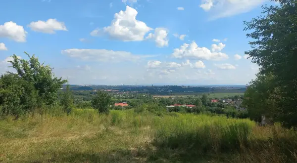Widok z góry św. Doroty na zieloną dolinę z domami i miastem w oddali. Błękitne niebo z białymi chmurami.