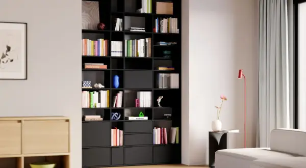 Moderne studio einrichtung mit schwarzem Regal voller Bücher und Deko-Objekte. Ein helles Sofa und ein roter Stehlampen ergänzen den Raum.