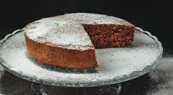 Torta al cioccolato soffice, una delizia senza farina e lievito, cosparsa di zucchero a velo su un'alzata di vetro.