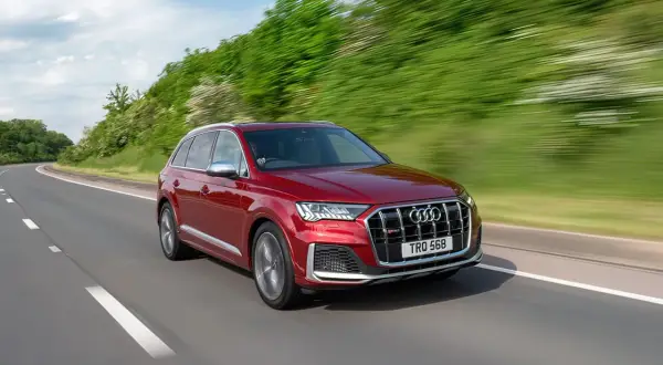 Czerwony Audi SQ7 pędzi po krętej drodze, otoczony zielenią.
