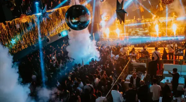 Multitud bailando en una discoteca con luces de neón, humo y una bola de discoteca, celebrando la nochevieja en Zaragoza.