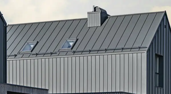 Nowoczesny dach na rąbek z dwoma oknami dachowymi i kominem. Elewacja z pionowych paneli metalowych i drewnianych elementów.