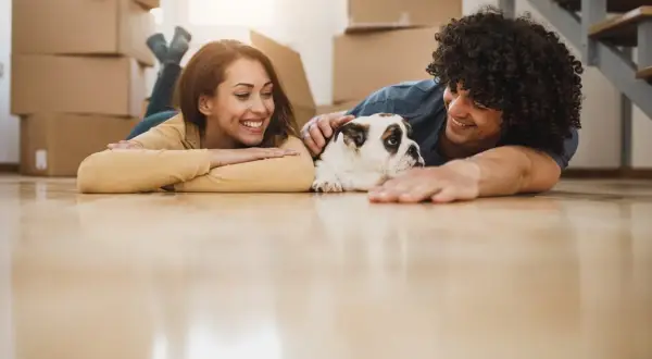 A happy couple and their bulldog relax on the floor amidst moving boxes, ready for their new home.