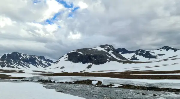 Snöklädda berg och en forsande älv i Jämtland, en vy som inspirerar till att bestiga Sylarna.