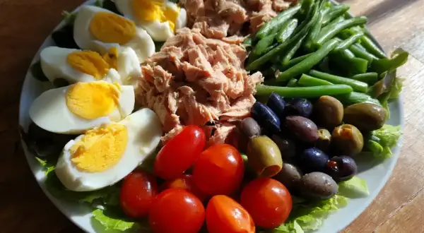 En härlig sallad nicoise med ägg, tonfisk, gröna bönor, tomater och oliver på en bädd av sallad.