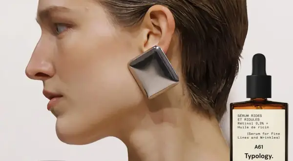 Frau mit auffälligem Ohrring und einem Fläschchen Retinol-Serum. Ab wann Retinol? Typology A61 für feine Linien.