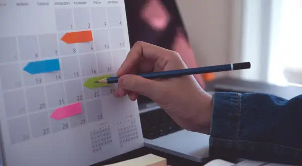 Kalender med färgglada post-it-lappar markerar viktiga datum. En hand med en penna planerar för bokslut enskild firma.