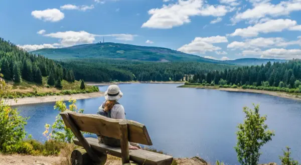 Frau auf Holzbank blickt auf See und bewaldete Berge im Harz.