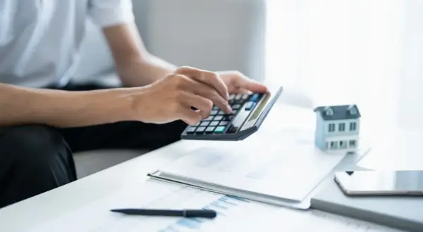 Man calculando la viabilidad hipoteca con calculadora, papeles y maqueta de casa.