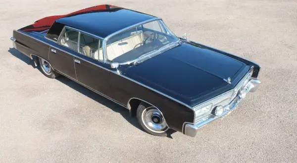 Svart imperial bil med kromdetaljer och ljus interiör, parkerad på grus. En klassiker som väcker beundran.