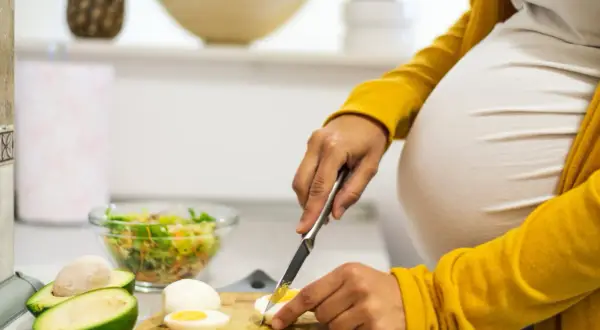 Schwangere bereitet gesunde Mahlzeit zu. Eier in der Schwangerschaft sind wichtig. Sie schneidet gekochtes Ei für Salat.