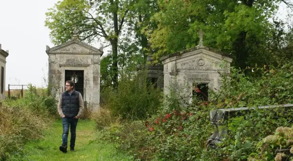 Un homme marche dans un cimetière abandonné en France, entouré de mausolées envahis par la végétation.