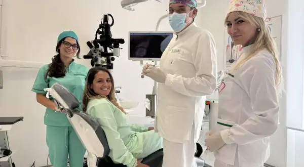Sorrisi in clinica: un dentista, due assistenti e una paziente felice. La prima visita dal dentista si paga, ma la salute orale è un investimento.