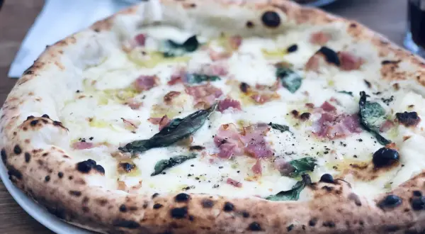 En ljuvlig pizza med bubblig lilla napoli deg, toppad med ost, bacon och basilika. Perfekt för en mysig kväll.