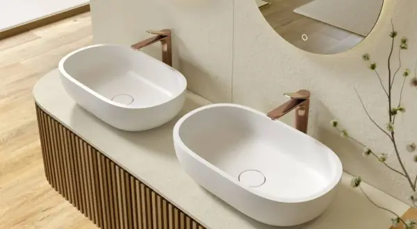 Due lavabi ovali bianchi su un mobile bagno su misura con finitura a listelli verticali. Rubinetteria color rame.
