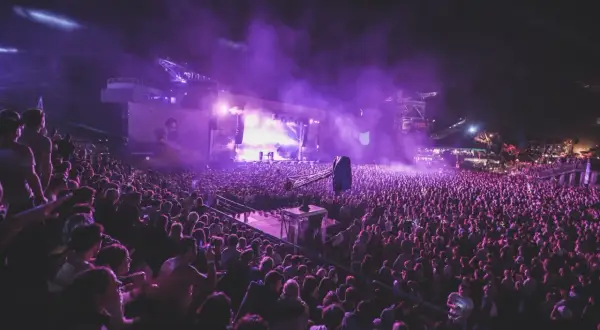 Tłum ludzi na nocnym koncercie, fioletowe światła i dym tworzą magiczną atmosferę. To niezapomniane u2 koncerty.