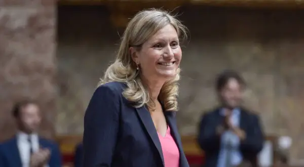 Une femme souriante, peut-être Vianney Pivet, d'origine inconnue, porte un blazer rayé et un haut rose.