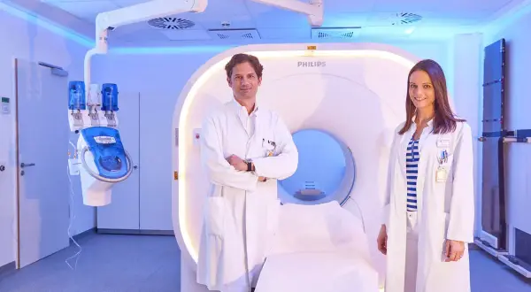 Zwei Ärzte, ein Nuklearmediziner und eine Kollegin, stehen vor einem modernen CT-Scanner.
