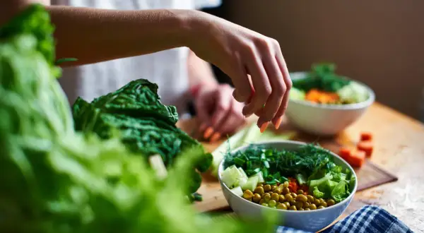 Mano che aggiunge erbe fresche a un'insalata colorata, ricca di fibre insolubili come piselli e verdure croccanti.
