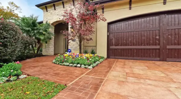 Stunning paver walkway ideas featuring a stamped concrete path leading to a home with a stone facade and a rich wooden garage door.