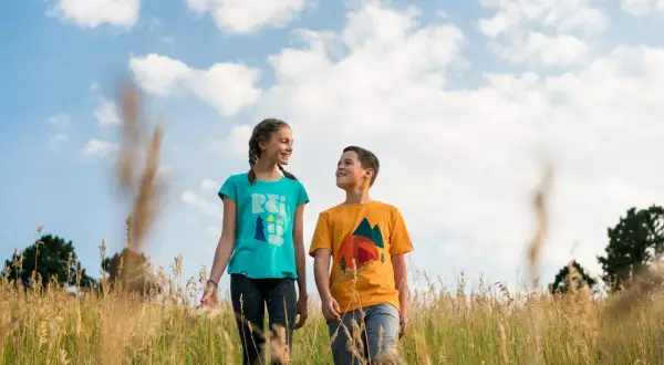 Two kids walk through a field of tall grass. A 50mm lens is good for capturing portraits like this, with a natural perspective and soft background blur.