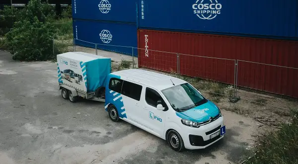Biały bus z przyczepą, na tle kontenerów. Zastanawiasz się nad prawem jazdy B+E koszt? To idealny zestaw do nauki.