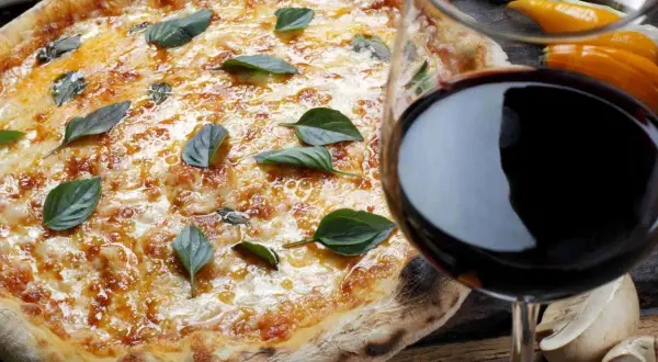 Pizza fumante con basilico e un bicchiere di vino rosso, il perfetto vino per pizza.