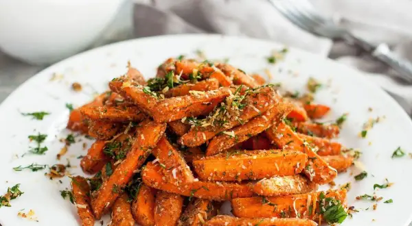 Karmelizowana marchewka, posypana ziołami i parmezanem, podana na białym talerzu.