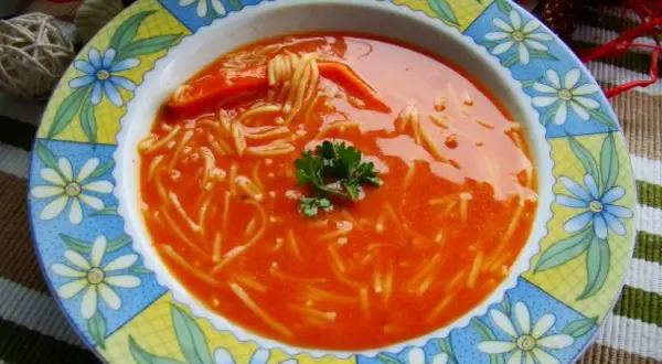 Zupa pomidorowa z przecieru z makaronem nitki i natką pietruszki, podana w kolorowym talerzu.