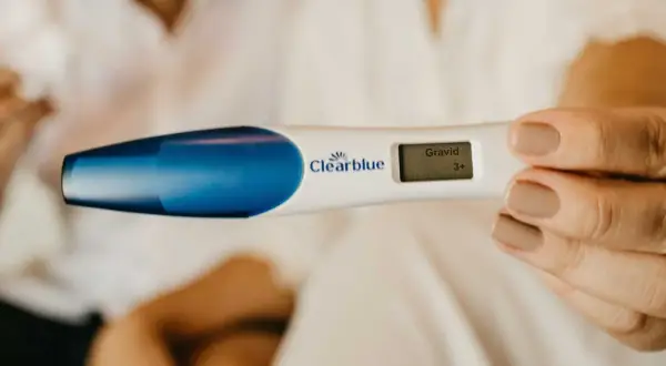 En hand håller ett digitalt graviditetstest som visar "Gravid 3+". Ett tidigt tecken på symtom på graviditet.
