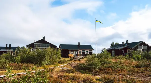 Mörka trähus med solpaneler och en svensk flagga som vajar vid ett vandrarhem i Dalarna.