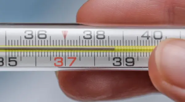Termometr pokazuje podwyższoną temperaturę ciała, około 37,5 stopnia Celsjusza.