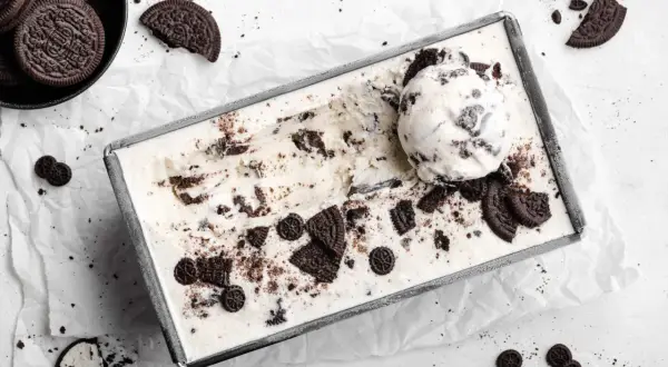 Selbstgemachtes Oreo Eis in einer Metallform, mit einem Löffel und zerbrochenen Keksen garniert. Perfekt für alle, die Oreo Eis selber machen wollen.