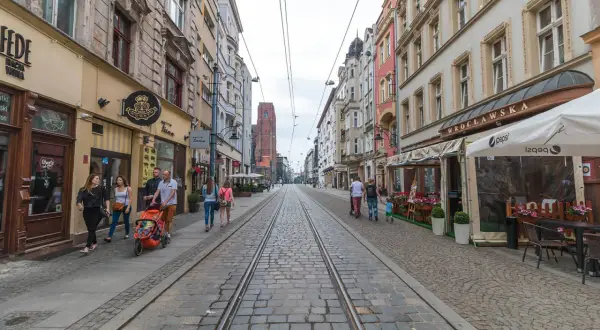 Spacer po starówce Wrocław, ulica z torami tramwajowymi i kamienicami. Rodzina z wózkiem spaceruje po bruku.