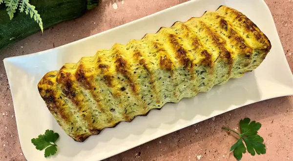 Un délicieux pain de courgettes, doré et savoureux, servi sur une assiette blanche. Parfait pour un repas léger.