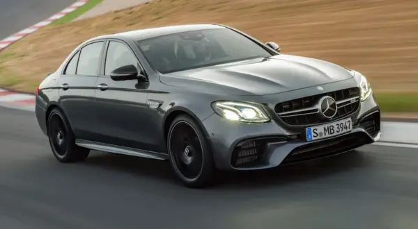 Szary Mercedes-Benz E63 AMG na torze wyścigowym, z kierowcą w kasku za kierownicą.