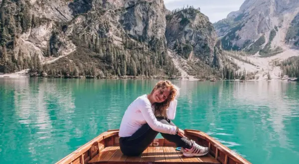 Kobieta w łodzi na tle turkusowego jeziora i górskiego krajobrazu Dolomitów.