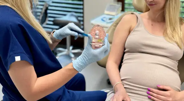 Dentystka pokazuje ciężarnej pacjentce model szczęki, omawiając higienę jamy ustnej. Piaskowanie zębów w ciąży jest bezpieczne i zalecane.