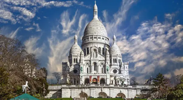 Bazylika Sacré-Cœur na wzgórzu Montmartre w Paryżu, z karuzelą w tle i dramatycznym niebem.