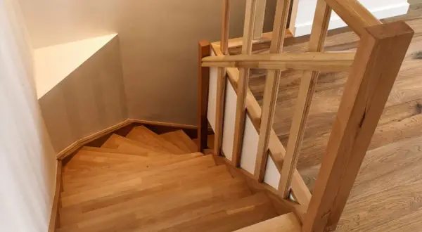 Holztreppe mit geschwungenen Stufen und einem hölzernen Geländer. Die Treppenstufen streichen das Licht und laden zum Hinaufgehen ein.