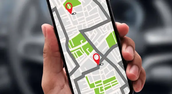 Dłoń trzyma smartfon z mapą i pinezkami. Dowiedz się, jak namierzyć telefon po numerze, by zawsze wiedzieć, gdzie jest bliska osoba.