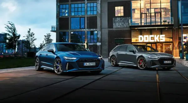 Dwa Audi RS6: niebieski sedan i szary Avant, zaparkowane przed budynkiem z napisem "DOCKS".