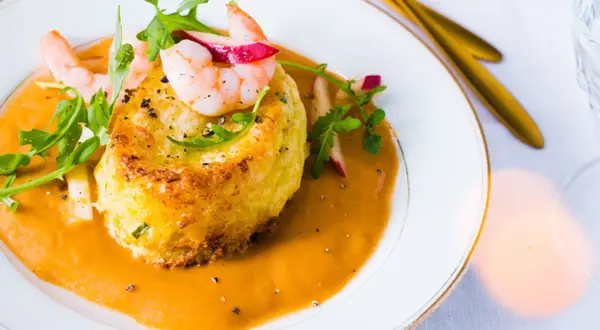 Un délicieux soufflé de crabe, nappé d'une bisque onctueuse et garni de crevettes et de roquette.