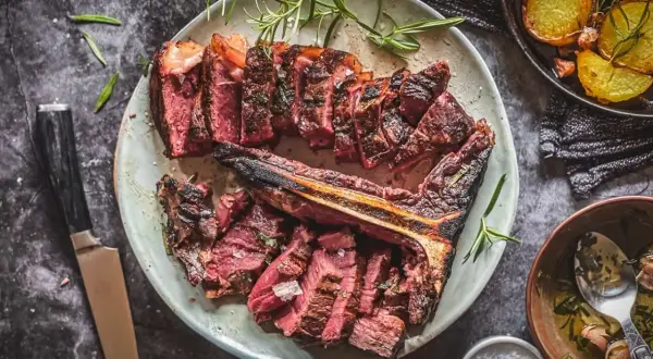 Aufgeschnittenes, perfekt gegrilltes Bistecca alla Fiorentina mit Rosmarin und Beilagen.
