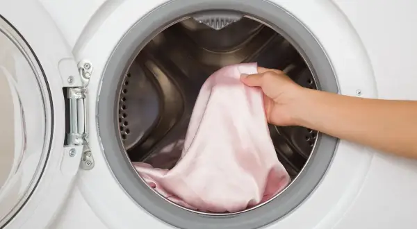 Mano inserisce un capo colorato in lavatrice. Ecco come lavare i capi colorati la prima volta per evitare che stingano.