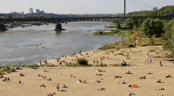 Słoneczna poniatówka nad Wisłą. Ludzie opalają się na piaszczystej plaży, w tle most i panorama Warszawy.