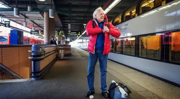 Äldre man i röd jacka på tågstationen, kanske på väg att resa som Kay Pollack.