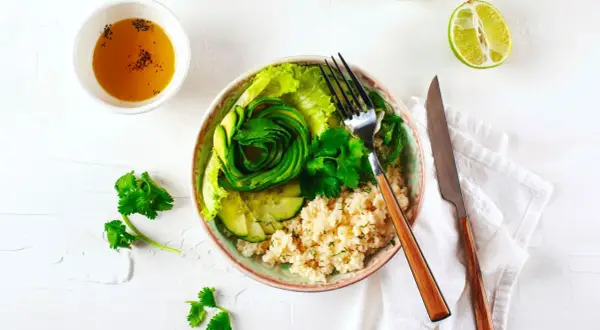 Un fresco e colorato cous cous freddo con avocado a spirale, cetrioli, lattuga e erbe aromatiche.